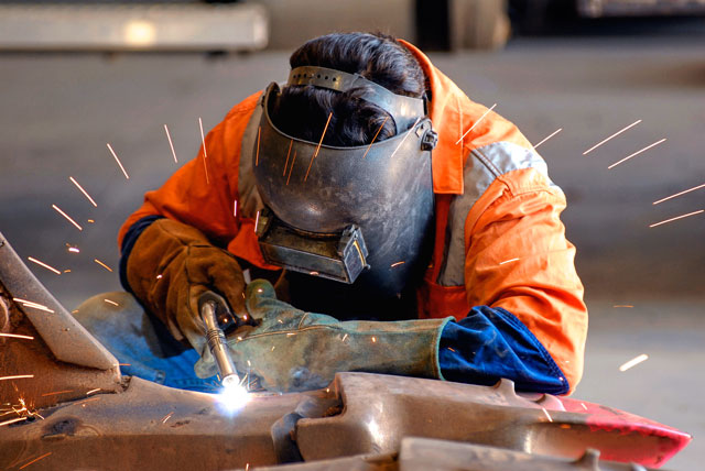 Welder in high-visibility gear welding heavy steel